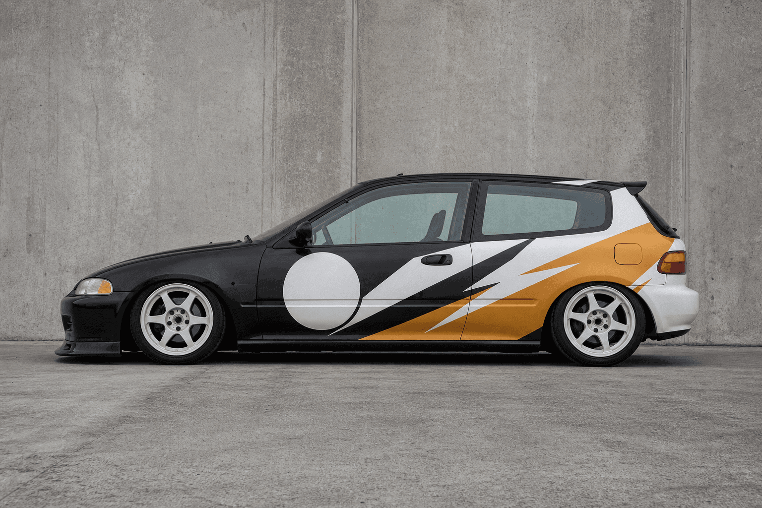 An original livery on a lowered import hatchback, photographed in daylight against a concrete wall.
